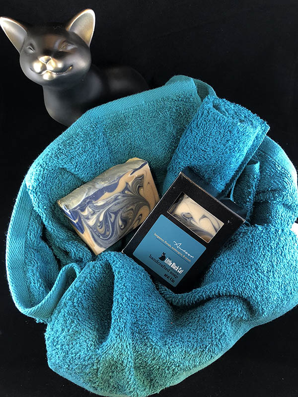 amazon soap bars, one in box one out, nested in a basket of teal towels with a sassy cat looking up at the viewer
